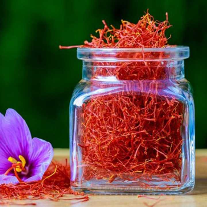 A glass jar filled with vibrant Iranian saffron threads, accompanied by a purple saffron flower.